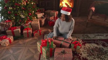 Mutlu Noeller Xmas. Afrikalı Amerikalı kadın Noel ağacının yanında hediye paketi hazırlıyor. Oturma odasında Noel ağacı ve şöminesi hediye paketi olan bir kız. Evde Noel arifesi