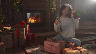 Mutlu noeller. Noel Baba şapkalı Afrikalı kadın akıllı telefondan görüntülü konuşma yapıyor. Sosyal ağda neşeli ruh hali kayıt videosu blogcusu. Noel 'i kutlamak için arkadaşlarıyla görüntülü görüşme yapan bir kız.