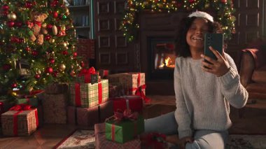 Mutlu noeller. Noel Baba şapkalı Afrikalı kadın akıllı telefondan görüntülü konuşma yapıyor. Sosyal ağda neşeli ruh hali kayıt videosu blogcusu. Noel 'i kutlamak için arkadaşlarıyla görüntülü görüşme yapan bir kız.