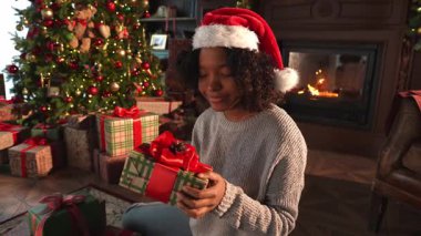 Mutlu Noeller Xmas. Afrikalı Amerikalı bir kadın Noel ağacının yanında hediye paketi veriyor. Oturma odasında Noel ağacı ve şömine ambalajlı hediye paketi olan bir kız. Evde Noel arifesi