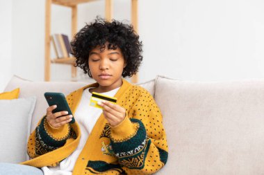 African american woman shopping online holding smartphone paying with gold credit card. Girl sitting at home buying on Internet enter credit card details. Online shopping ecommerce delivery service
