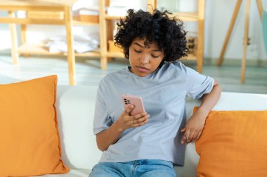 African girl holding smartphone touch screen typing scroll page at home. Woman with cell phone surfing internet using social media apps playing game. Shopping online Internet news cellphone addiction