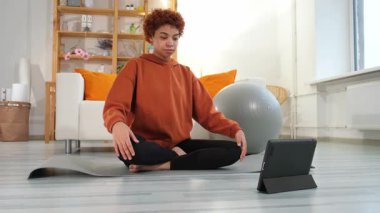 Yoga mindfulness meditation. Young healthy african girl practicing yoga at home. Woman sitting in lotus pose on yoga mat eyes close hands in prayer meditating indoor. Girl doing breathing practice