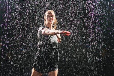 Siyah arka planda yağmur suyunda poz veren çağdaş kadın dansçı. Dişi sanatçı ifade ile dans ediyor. Modern balerin karanlıkta dans ediyor. Tutku karanlıkta dans eder. Esneklik dengesi