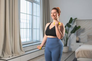 Fitness antrenmanı. Dambılları kaldıran kadın. Artı ev içinde spor egzersizi yapan beden bir kadın. Spor giyimli kız kilo vermek için ağırlık çalışması yapıyor. Spor ve zindelik