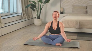 Yoga farkındalığı meditasyonu. Evde yoga yapan bir kadın. Artı nilüfer çiçeğinin üzerinde oturan kadın meditasyon yapıyor içeride rahatlarken gülümsüyor. Nefes egzersizi yapan bir kız. Evde yoga.