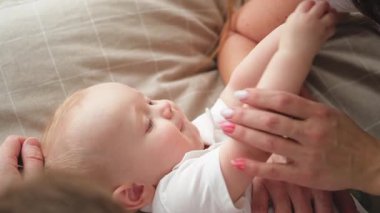 Evde mutlu bir aile. Anne baba, küçük bebekle yatakta oynuyor. Anne, baba, bebek, rahatlayın ve birlikte eğlenin. Bir kadın bebeğe sevgiyle sarılıyor. Bebeği emziriyor.