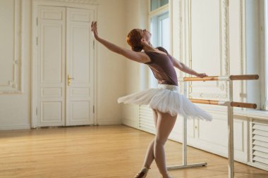 Tutu etekli genç balerin dans sınıfında bale pozisyonlarında dans ediyor. Dans stüdyosundaki genç klasik dansçı kadın. Bale sınıfı eğitim konsepti