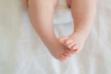 Minik bebek ayakları ve ayak parmakları beyaz arka planda. Beyaz battaniyenin altında yeni doğmuş bebek bacakları. Bebek yalınayak yaklaşın. Annelik şefkati ebeveynlik doğum günü. Mutlu Aile