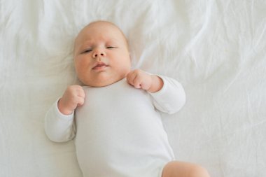 Mutlu bebek. Yatak odasında, gülümseyen yüzüyle küçük şirin bir kız. Bebek dinleniyor, evde beyaz battaniyeye uzanmış oynuyor. Annelik mutlu çocuk bakımı konsepti