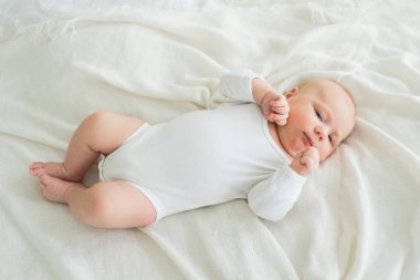 Mutlu bebek. Yatak odasında, gülümseyen yüzüyle küçük şirin bir kız. Bebek dinleniyor, evde beyaz battaniyeye uzanmış oynuyor. Annelik mutlu çocuk bakımı konsepti