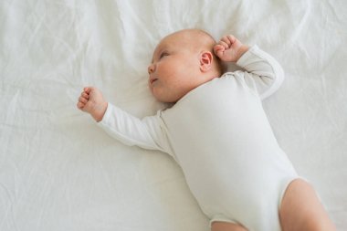 Mutlu bebek. Yatak odasında, gülümseyen yüzüyle küçük şirin bir kız. Bebek dinleniyor, evde beyaz battaniyeye uzanmış oynuyor. Annelik mutlu çocuk bakımı konsepti
