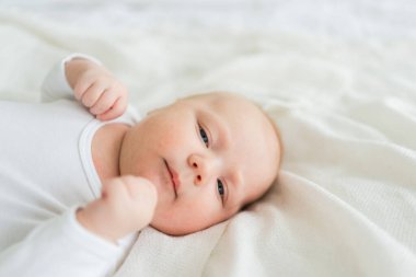 Mutlu bebek. Yatak odasında, gülümseyen yüzüyle küçük şirin bir kız. Bebek dinleniyor, evde beyaz battaniyeye uzanmış oynuyor. Annelik mutlu çocuk bakımı konsepti