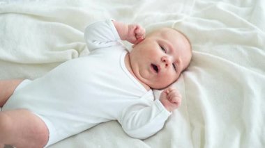 Mutlu bebek. Yatak odasında, gülümseyen yüzüyle küçük şirin bir kız. Bebek dinleniyor, evde beyaz battaniyeye uzanmış oynuyor. Annelik mutlu çocuk bakımı konsepti