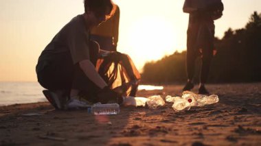 Dünya günü. Gönüllü eylemciler sahil bölgesindeki çöpleri topluyor. Kadınlar ve erkekler okyanus kıyısındaki çöp torbasına plastik çöp koyar. Çevre koruma kıyı bölgesi temizliği
