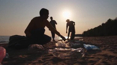 Dünya günü. Gönüllü eylemciler sahil bölgesindeki çöpleri topluyor. Kadınlar ve erkekler okyanus kıyısındaki çöp torbasına plastik çöp koyar. Çevre koruma kıyı bölgesi temizliği