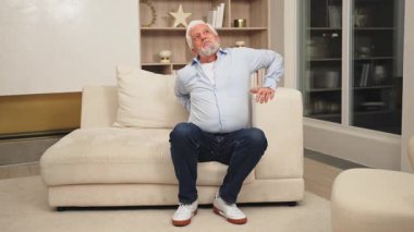 Sırt ağrısı. Memnuniyetsiz yaşlı adam evde sırt ağrısı çekiyor. Yaşlı adam aniden sırt ağrısı hisseder kaslar gerilim yaralanması. Üzgün büyükbaba sırtı ağrıyan omurgaya dokunuyor.