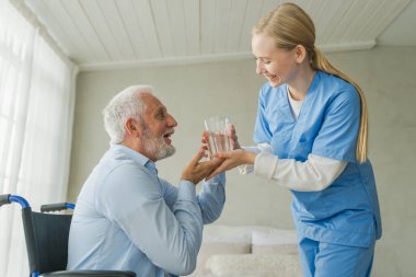 Sağlık hizmetleri su dengesini desteklemeye yardımcı olur. Hemşire tekerlekli sandalyedeki yaşlı adam için cam su veriyor. Engelliler için tekerlekli sandalyedeki felçli adam taze su içiyor. Kıdemli adam ve hemşire evde.