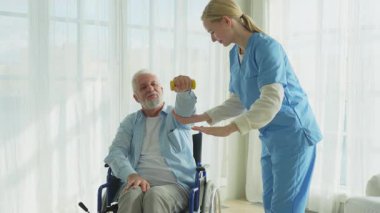 Rehabilitasyon sağlık hizmetlerini destekleyin. Hemşire, tekerlekli sandalyedeki yaşlı hastaya dambılları toplamasında yardım ediyor. Engelli insanlar için tekerlekli sandalyede oturan sakat bir adam hemşireyle spor egzersizi yapıyor. Tıbbi bakıcı.