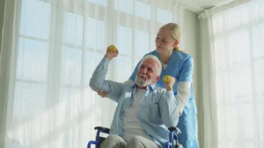 Rehabilitasyon sağlık hizmetlerini destekleyin. Hemşire, tekerlekli sandalyedeki yaşlı hastaya dambılları toplamasında yardım ediyor. Engelli insanlar için tekerlekli sandalyede oturan sakat bir adam hemşireyle spor egzersizi yapıyor. Tıbbi bakıcı.