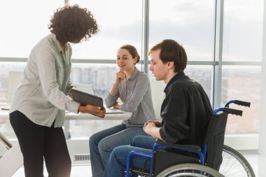 Takım çalışması beyin fırtınası. Çeşitli çok ırklı meslektaşlar birlikte çalışan engelli insanlar için sandalyede oturuyor. Yaratıcı ofiste oturup iş konuşan bir grup insan. Genç profesyonel takım