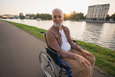 Tekerlekli sandalyedeki mutlu son sınıf öğrencisi gülümseyerek şehir parkında özgürlüğün tadını çıkarıyor. Engelliler için sandalyedeki yaşlı, neşeli, pozitif adam. Engelli hastalıkları rehabilitasyonu