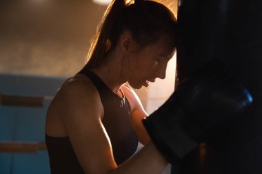 Kadın kendini savunma gücü. Boks ringinde dövüşten sonra dinlenen güçlü kadın boksör. Güçlü kız boks torbasını yumrukladıktan sonra yoruldu. Spor salonunda eğitim günü. Vücut çalıştırma eğitimine uygun güç
