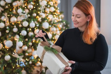 Mutlu noeller. Noel ağacının yanındaki hediye kutusunu açan kadın. Oturma odasında elinde Noel ağacı olan sürpriz suratlı bir hediye kutusu tutan bir kız. Noel arifesini evde kutlayan kadın