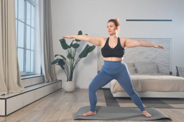 Yoga fitness antrenmanı. Evde yoga yapan bir kadın. Artı ev içinde yoga minderiyle spor egzersizi yapan beden bir kadın. Spor giyim bölümündeki kız kilo vermek için antrenman yapıyor. Spor ve zindelik