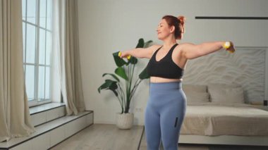 Fitness antrenmanı. Dambılları kaldıran kadın. Artı ev içinde spor egzersizi yapan beden bir kadın. Spor giyimli kız kilo vermek için ağırlık çalışması yapıyor. Spor ve zindelik