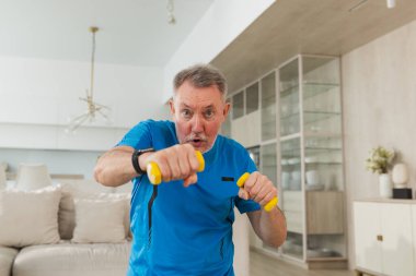 Fitness antrenmanı. Üst düzey boksör dambılları kaldırıyor. Yetişkin, sağlıklı bir adam evde spor yapıyor. Büyükbabanın rehabilitasyonu var. Sağlık hizmetleri sağlıklı yaşam tarzı