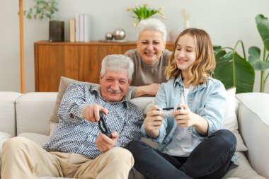 Evde mutlu bir aile. Yaşlı adam büyükbaba kadın büyükanne kız torun evde joysticklerle oyun oynuyor. Oyun için gamepad kullanan iki nesil büyükbaba ve ergen