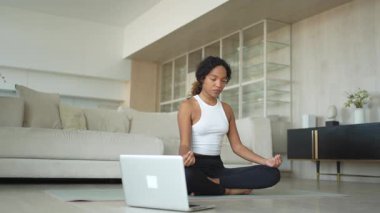 Yoga farkındalığı meditasyonu çevrimiçi. Afrikalı kadın evdeki bilgisayarında online derslerle yoga yapıyor. Lotus 'ta oturan kadın meditasyon yapıyor. Nefes egzersizi yapan bir kız. Evde yoga.