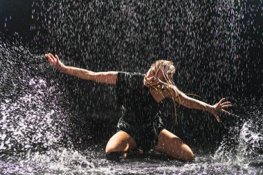 Siyah arka planda yağmur suyunda poz veren çağdaş kadın dansçı. Dişi sanatçı ifade ile dans ediyor. Modern balerin karanlıkta dans ediyor. Tutku karanlıkta dans eder. Esneklik dengesi