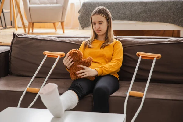 Kanepede oturan kırık bacaklı genç kız. Üzgün küçük çocuk, kırık bacağını iyileştirmek için oyuncak ayısına sarılıyor. Alçı ve koltuk değneği kullanan bir kız. Kaza sonucu oluşan kırık, ayak bandajı.