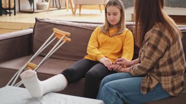 Kırık bacağı alçıda olan bir kız evde kanepede annesiyle oturuyor. Kırık bacağı iyileşen üzgün genç bir çocuk. Hızlı rehabilitasyon için koltuk değneklerini kullanan bir kız. Anne destek kızı