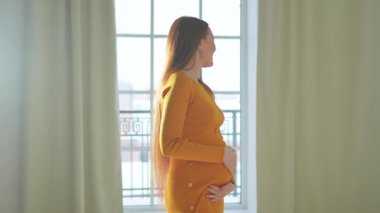 Hamilelik anneliği insanların gelecek beklentisi. Evinin penceresinin yanında koca göbekli hamile bir kadın var. Karnına sarılan ve hamileliğin tadını çıkaran bir kız. Annelik şefkati ebeveynlik yeni yaşam konsepti