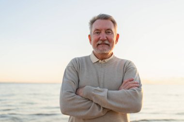 Sahilde kendine güveni tam orta yaşlı bir Avrupalı 'nın açık hava portresi. Yaşlı, olgun bir adam gülümsüyor. Mutlu büyükbaba kameraya bakıyor. Yüz portresi yakın çekim. Mutlu insanlar.