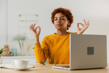 Stres yok, sakin ol. Dikkatli Afrikalı iş kadını ev ofisinde nefes alma egzersizleri yapıyor. İş yerindeki barışçıl genç kadın yoga yaparken gözleri kapalı çene mudra hareketinin tadını çıkarıyor. Ofis meditasyonu