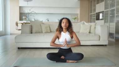 Yoga farkındalığı meditasyonu. Genç sağlıklı Afrikalı kız evde yoga yapıyor. Lotus 'ta oturan kadın yoga minderinde poz veriyor içeride meditasyon yapıyor. Nefes egzersizi yapan bir kız. Evde yoga.