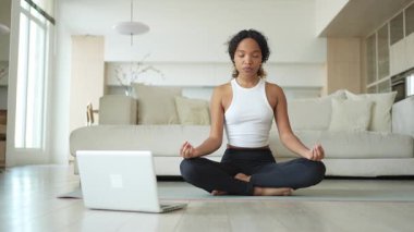 Yoga farkındalığı meditasyonu çevrimiçi. Afrikalı kadın evdeki bilgisayarında online derslerle yoga yapıyor. Lotus 'ta oturan kadın meditasyon yapıyor. Nefes egzersizi yapan bir kız. Evde yoga.
