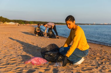 Dünya günü. Gönüllü eylemciler, sahil bölgesindeki çöpleri topluyor. Kadınlar okyanus kıyısındaki çöp torbasına plastik çöp koyar. Çevre koruma kıyı bölgesi temizliği