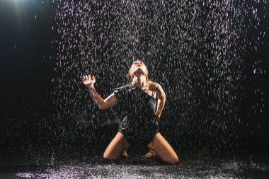 Siyah arka planda yağmur suyunda poz veren çağdaş kadın dansçı. Dişi sanatçı ifade ile dans ediyor. Modern balerin karanlıkta dans ediyor. Tutku karanlıkta dans eder. Esneklik dengesi