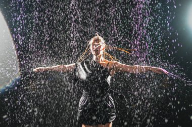 Siyah arka planda yağmur suyunda poz veren çağdaş kadın dansçı. Dişi sanatçı ifade ile dans ediyor. Modern balerin karanlıkta dans ediyor. Tutku karanlıkta dans eder. Esneklik dengesi