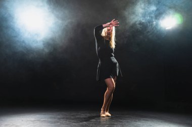 Siyah arka planda dumanla poz veren çağdaş kadın dansçı. Yetişkin kadın sanatçı ifade ile dans ediyor. Modern balerin karanlıkta dans ediyor. Tutku karanlıkta dans eder. Esneklik dengesi