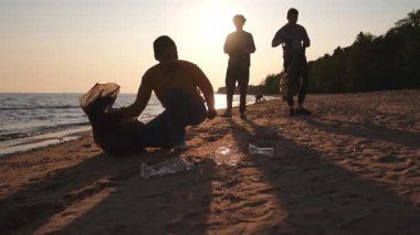 Dünya günü. Gönüllü eylemciler sahil bölgesindeki çöpleri topluyor. Kadınlar ve erkekler okyanus kıyısındaki çöp torbasına plastik çöp koyar. Çevre koruma kıyı bölgesi temizliği