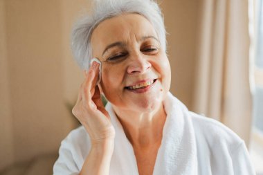 Yetişkin, yaşlı bir kadın günlük güzellik rutini yapıyor pamukla makyaj yapıyor. Losyon süngerli yaşlı kadın yüz bakımı yaptırıyor. Cilt bakımı yaşlandırıcı cilt temizleyici