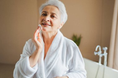 Yetişkin, yaşlı bir kadın günlük güzellik rutini yapıyor pamukla makyaj yapıyor. Losyon süngerli yaşlı kadın yüz bakımı yaptırıyor. Cilt bakımı yaşlandırıcı cilt temizleyici