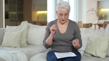 Üzgün, hasta, yalnız yaşlı kadın evde yalnız başına kötü haberler okuyor. Mutsuz, olgun bir büyükanne, kederli, göreceli bir ölüm yaşıyor. Kağıt döküman faturası olan stresli yaşlı kadın