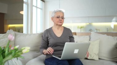 Orta yaşlı yaşlı bir kadın evde, ellerini ve vücudunu dinlendirip laptopta işe ara veriyor. Yaşlı, olgun bir kadın işten sonra mutlu olur. Uzun dizüstü bilgisayar kullanımından dolayı yorgunluk